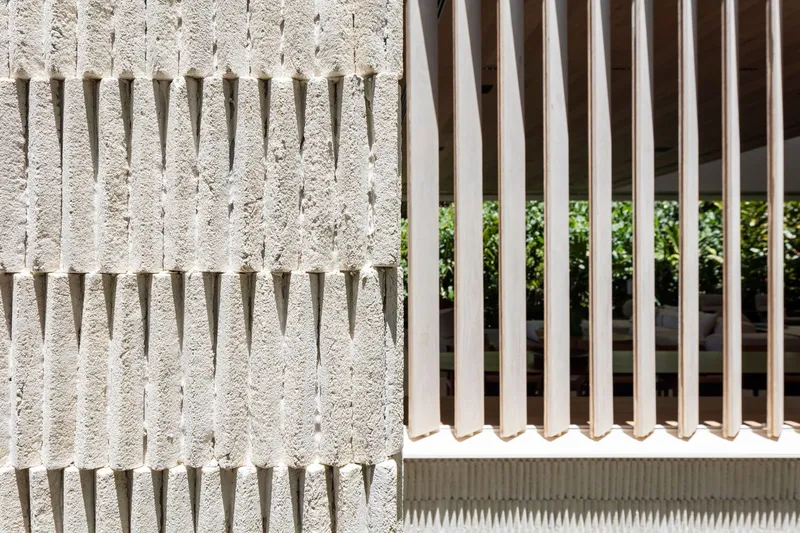 Textured concrete wall with projecting dowels beside a white vertical fin screen in sunlight