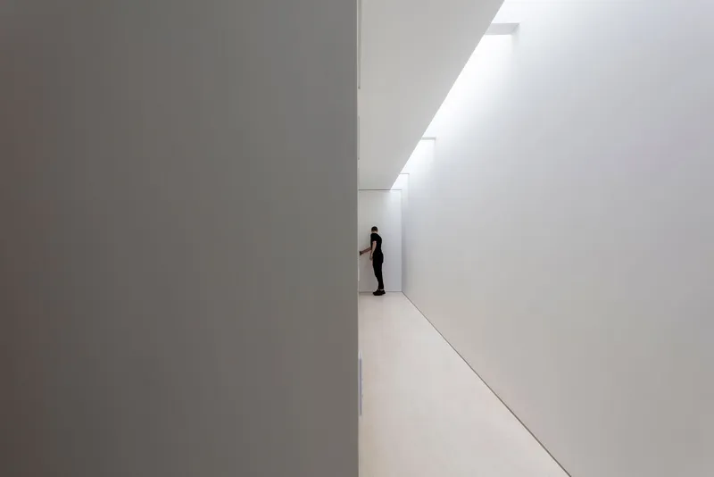 White corridor with a single figure standing at the far end beneath a clerestory window