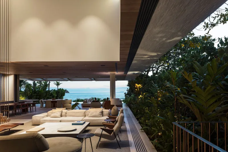 Living area with deep overhang and timber ceiling opening to planted garden and sea view