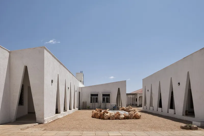 Central courtyard: white plastered walls with triangular window openings on both sides, local rocks at centre, blue desert sky