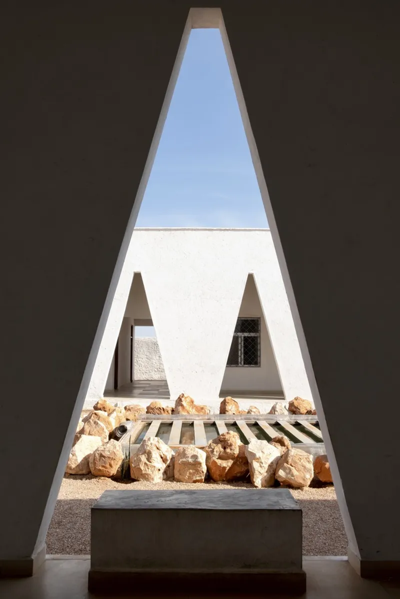 View through triangular window: courtyard rocks and opposite building wall framed by the deep plastered reveal