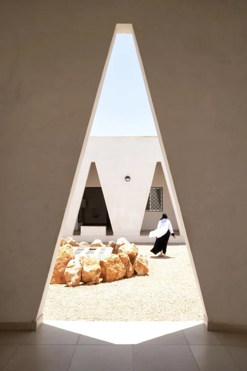 Through a triangular window: courtyard with rocks and a figure visible, bright light framing the deep reveal