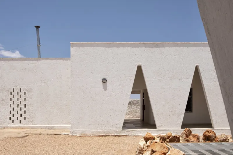 Exterior: white wall with two triangular openings, perforated brick ventilation screen, wind tower chimney rising above