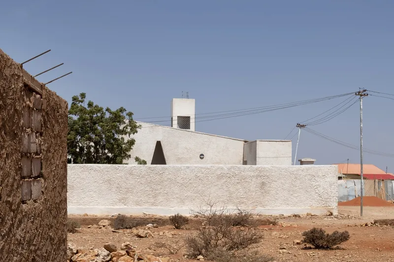 Town context: white hospital with wind tower visible above a traditional stone boundary wall, power line, dry landscape
