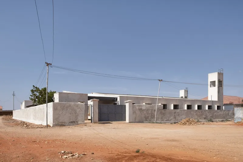 Street view: hospital entrance with perforated brick screen wall, metal gate, wind tower rising above