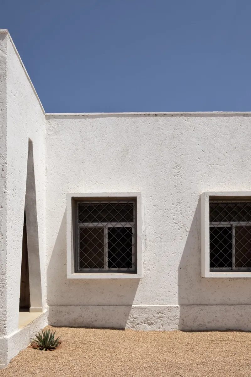 Triangular window detail: deep plastered reveal casting sharp shadow, white wall, blue sky above