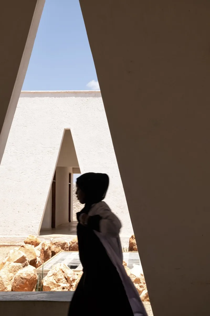Silhouette: figure framed in a triangular window, courtyard and opposite building visible beyond