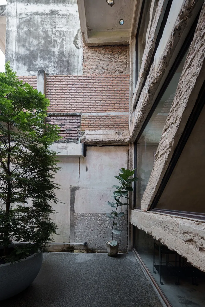 Ground floor full view: concrete bar, exposed ductwork, peeled plaster revealing brick, stair with glass balustrade, bottle display wall