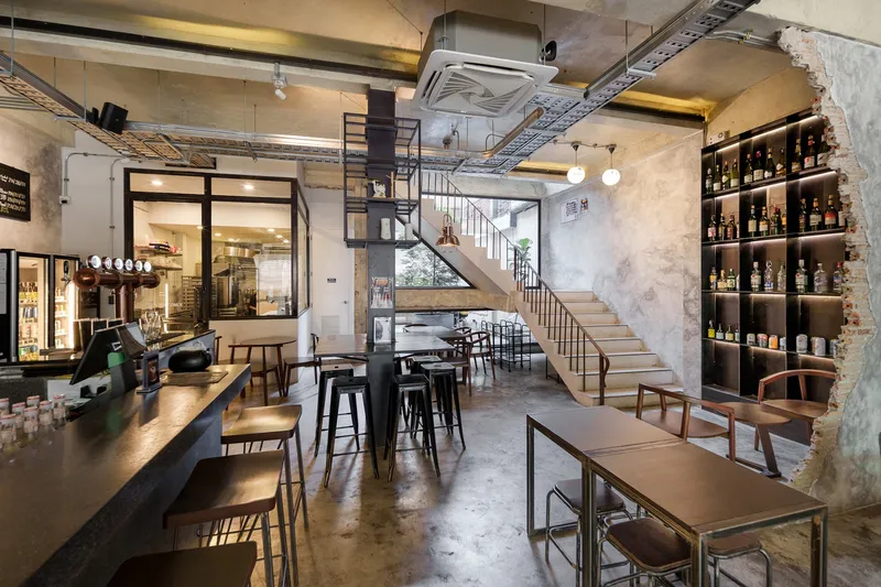 Ground floor evening: full bakery counter with underlit display, shelving, pendant lamps, stair in background