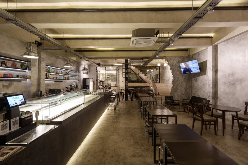 Under the stair: concrete stringer, bottle display shelving on raw brick, metal bar tables, timber seating