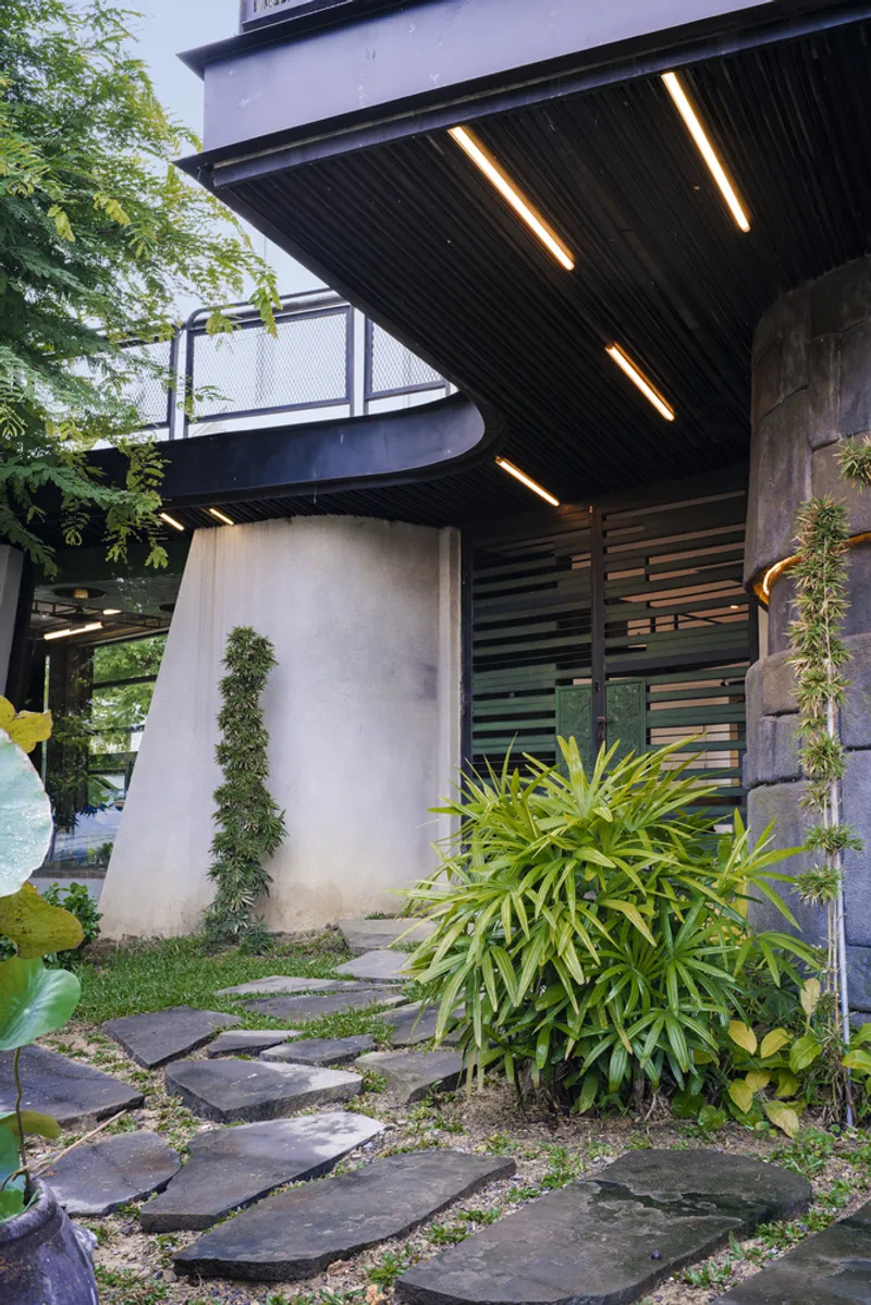 Covered entry with linear ceiling lights, concrete columns and irregular stepping stones through planted beds