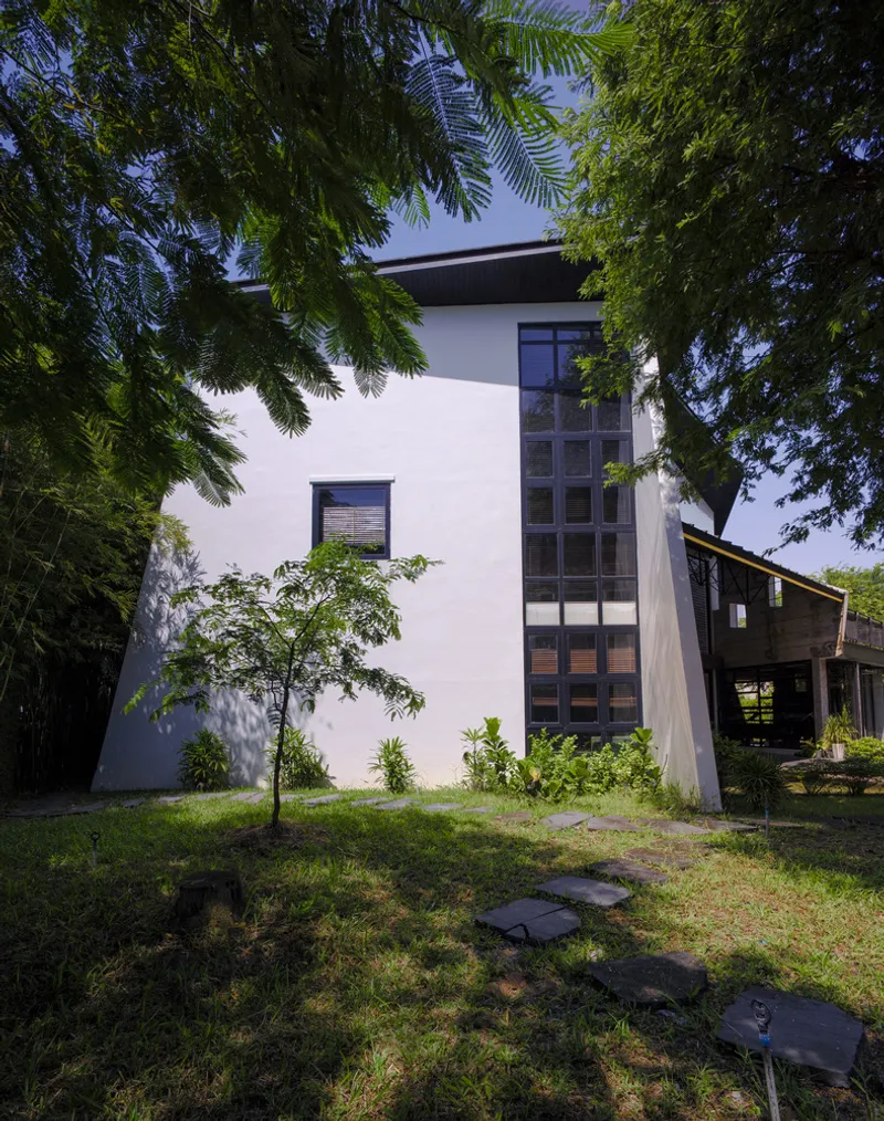 White stucco facade with vertical ribbon window framed by overhanging trees and stepped stone path