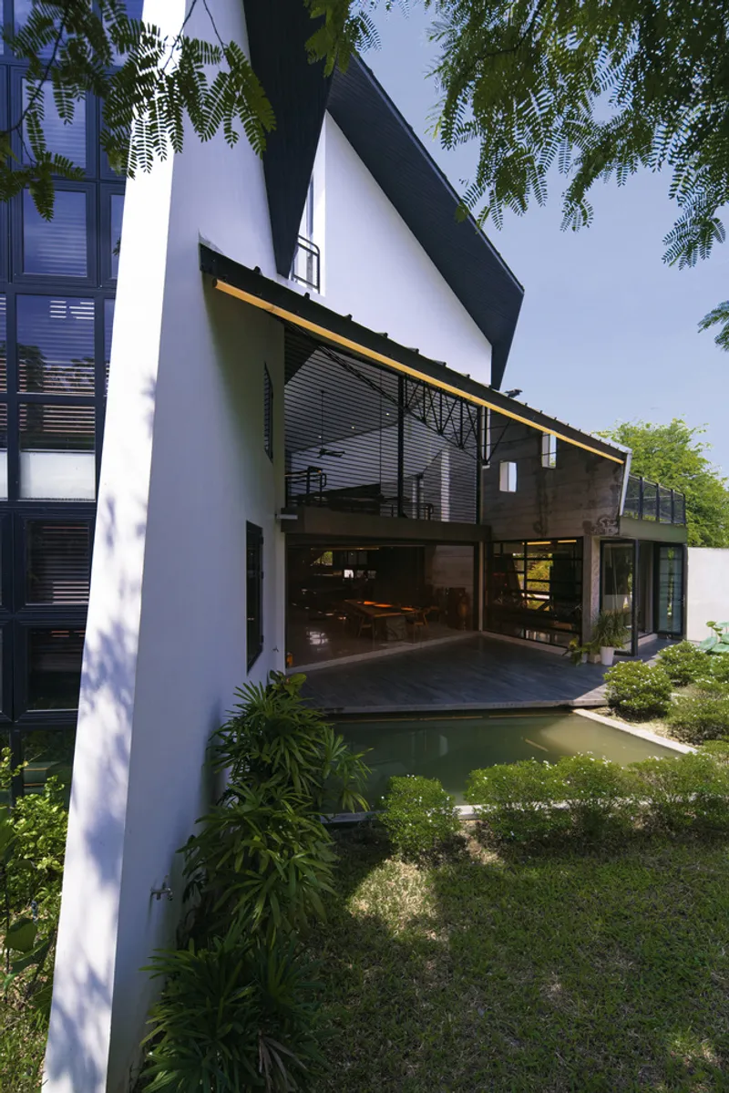 Garden courtyard with reflecting pool and open louvered facade beneath cantilevered upper volume in midday sun