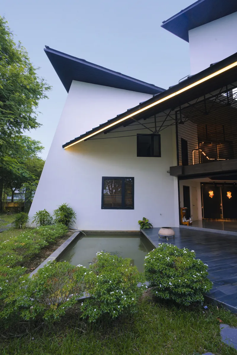 White rendered facade with angular black rooflines overlooking a courtyard garden and reflecting pool at dusk