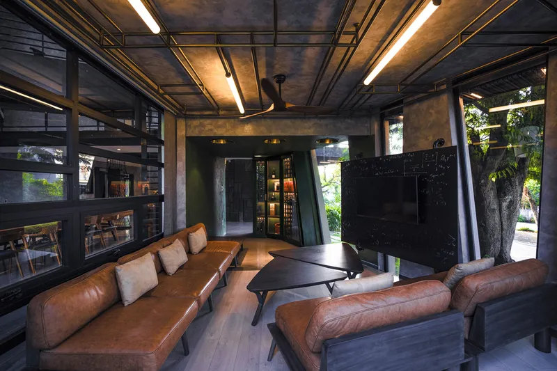 Double-height lounge with exposed concrete ceiling grid and tan leather sofas facing glass doors to a garden
