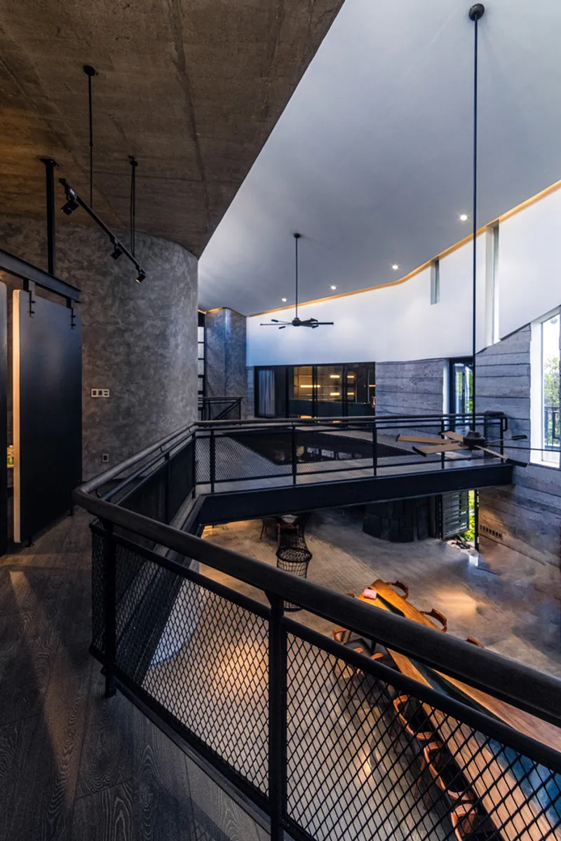 Mesh-floored mezzanine bridge crossing a central void with exposed concrete soffit and white plaster walls