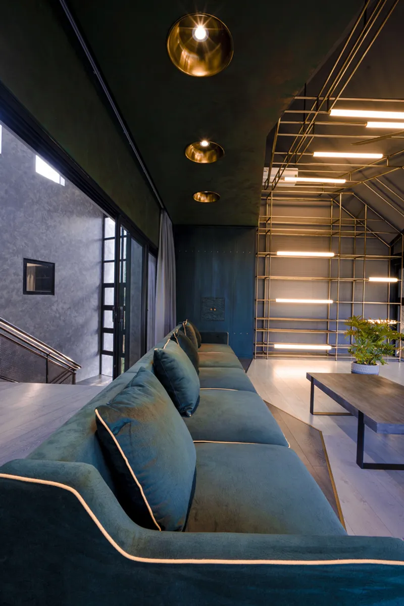 Living room with teal upholstered sofa beneath exposed brass tube lighting and gold pendant fixtures
