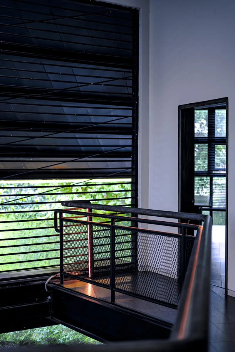 Interior view of the metal mesh balcony railing with horizontal louvered window opening to greenery