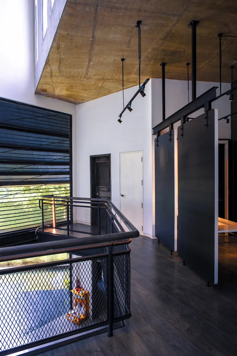 Upper landing space with exposed plywood ceiling and black pendant track lights above the mesh balustrade