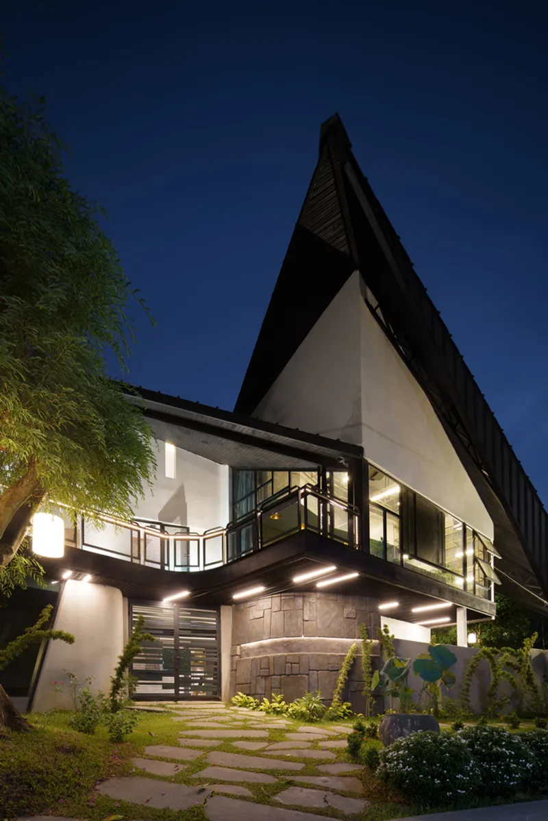 Entrance facade at dusk with angular metal roof overhang and stone base wall beneath balcony