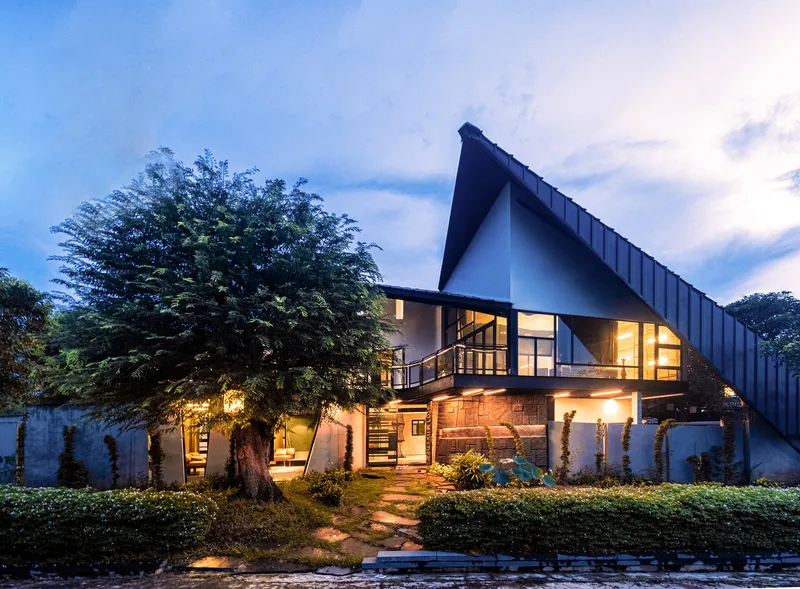 Garden elevation at twilight with large tree beside the stone base and illuminated interior spaces