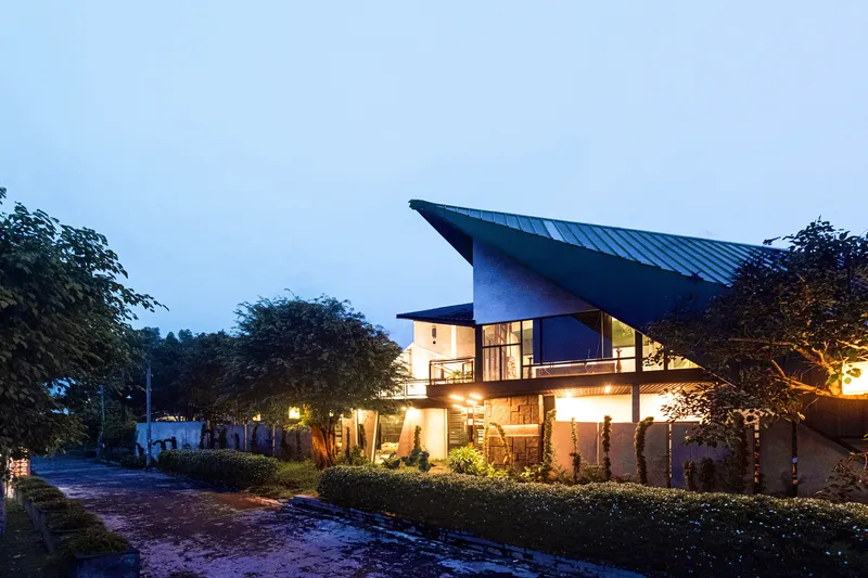 Street view at dusk showing the pitched metal roof and planted hedge along the property edge