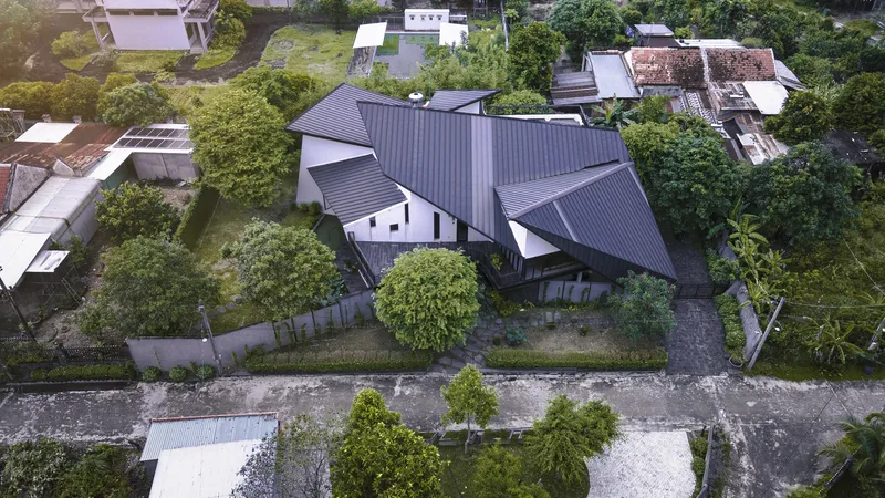 Aerial view of the multi-gabled corrugated metal roof surrounded by trees and neighboring houses