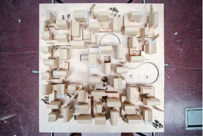 Aerial photograph of the wooden physical model: a dense grid of small pitched-roof houses on a square base with a central plaza and two oval public spaces