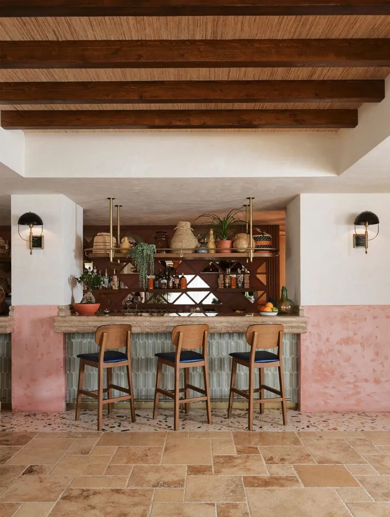 Kitchen bar with pink plaster base and three timber stools beneath exposed timber beam ceiling