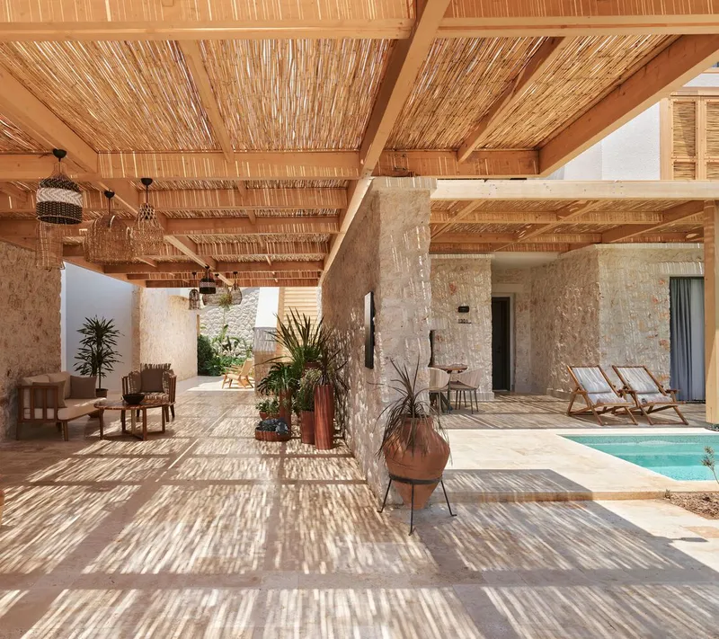 Covered terrace with exposed timber beams and reed ceiling casting dappled shadows across stone flooring