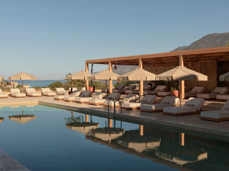 Poolside deck with timber-frame shade structure and canvas umbrellas overlooking the sea at dusk