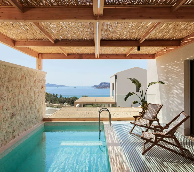 Private plunge pool under reed and timber pergola with stone wall and coastal views beyond
