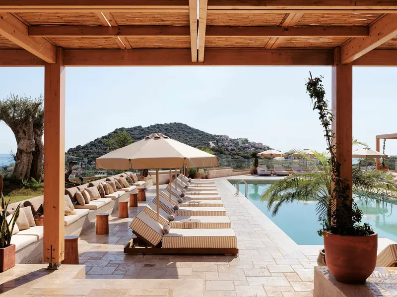 Poolside terrace with timber pergola, striped loungers, and planted pots facing distant hillside landscape