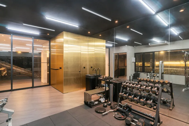 Fitness room with golden glass-clad sauna cube, black ceiling and rows of free weights
