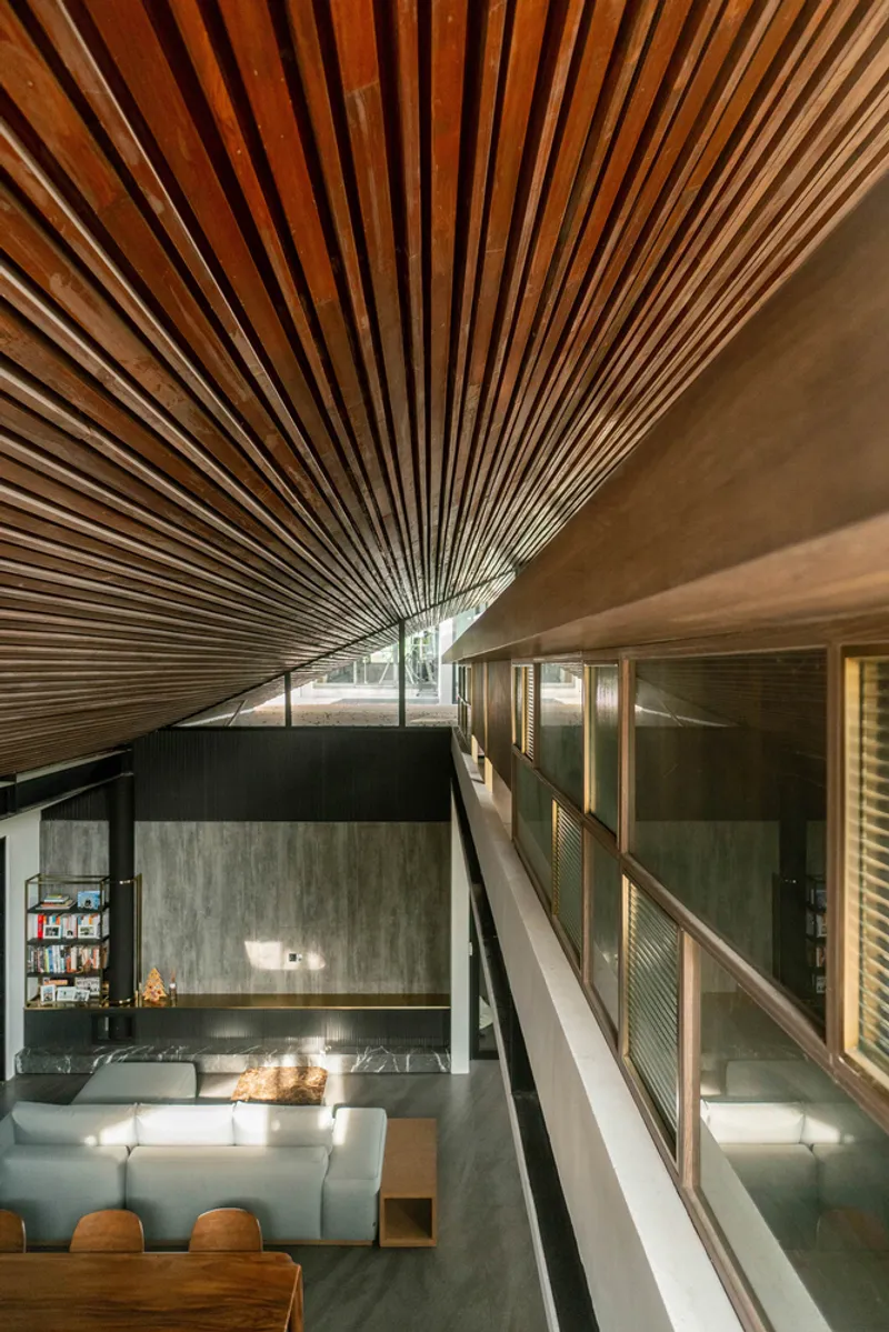 Double-height living space with radiating timber slat ceiling above concrete walls and mezzanine walkway