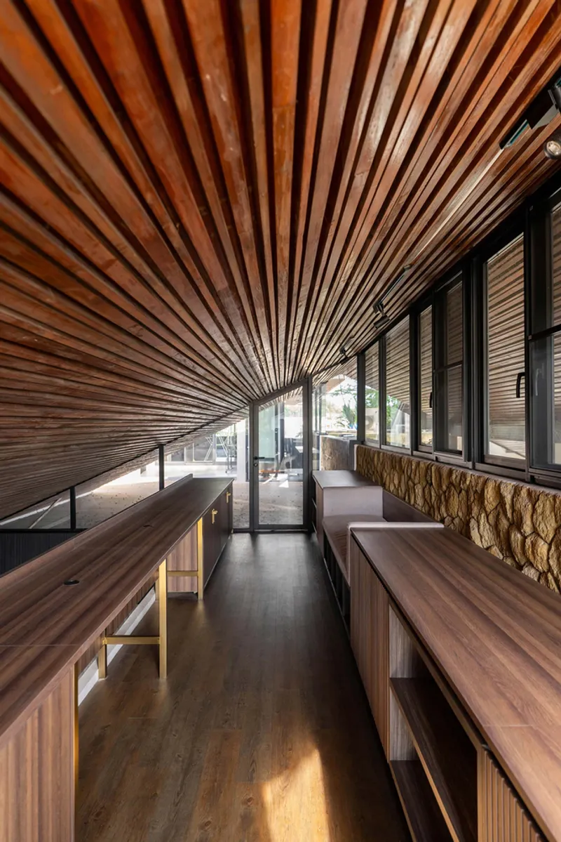 Upper-level corridor with radiating timber slat ceiling and stone feature wall under natural daylight