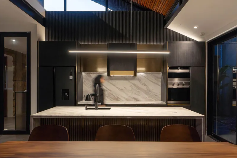 Kitchen island with marble backsplash and black cabinetry beneath a linear suspended light fixture at dusk