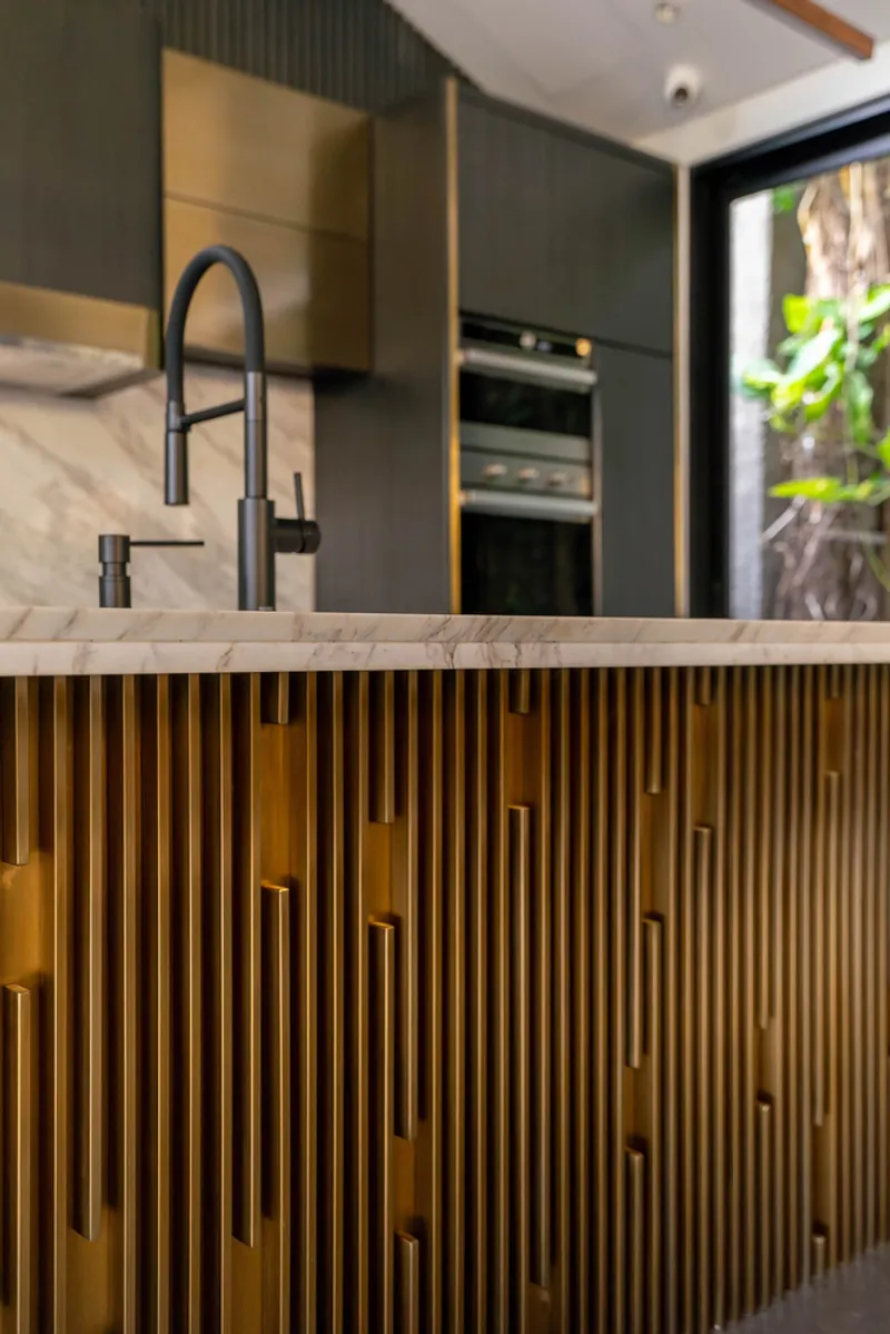 Kitchen island with vertical brass slat panels and black matte faucet at marble countertop