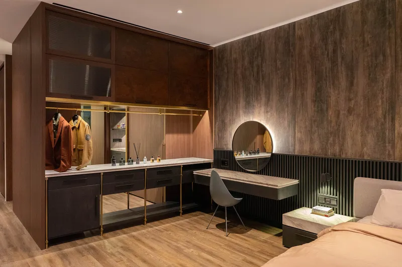 Bedroom dressing area with dark wood wardrobe and circular backlit mirror above fluted panel vanity desk