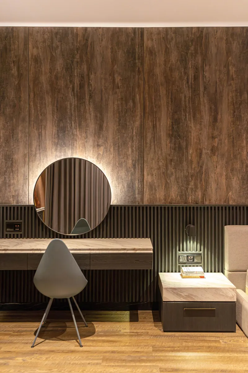 Vanity desk with round illuminated mirror against weathered timber wall and ribbed black wainscot panel