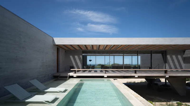 Pool courtyard: turquoise plunge pool between concrete walls, white loungers, timber pergola casting shadow lines, dunes visible beyond