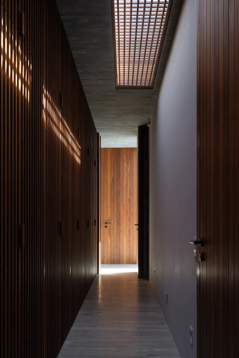 Corridor: dark timber slatted walls, lattice ceiling filtering daylight, door at the far end, moody interior light