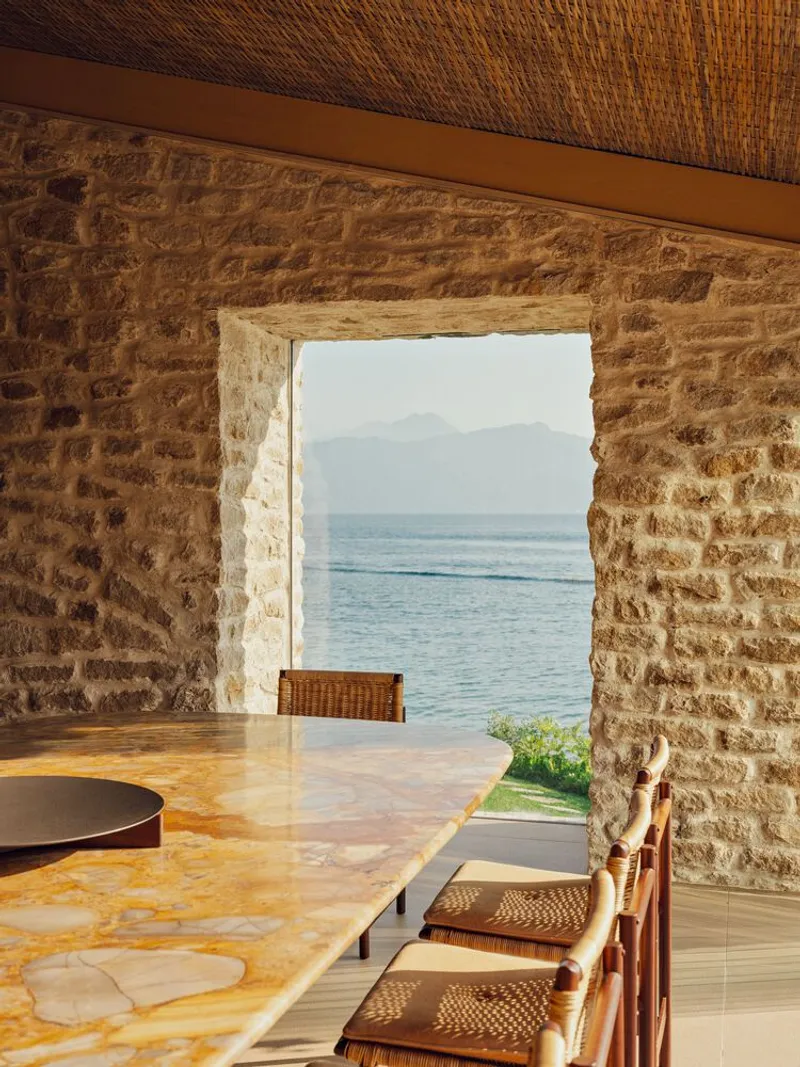 View through stone opening framing the lake with woven ceiling and stone table edge