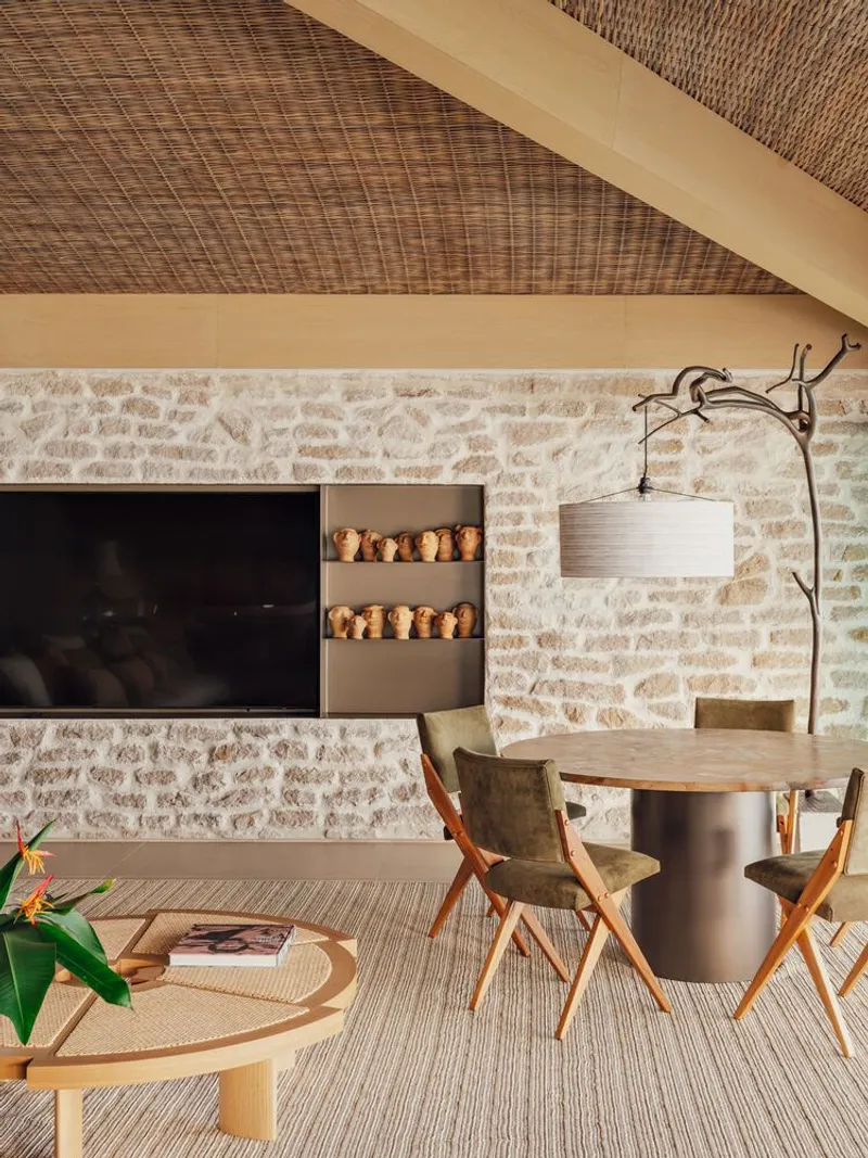 Living area with woven rattan ceiling, limestone wall, built-in shelves with ceramic pots, and timber beam
