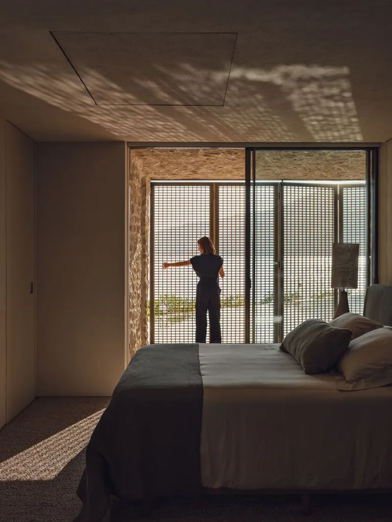 Bedroom with a person at sliding glass doors casting dappled shadow patterns across the ceiling