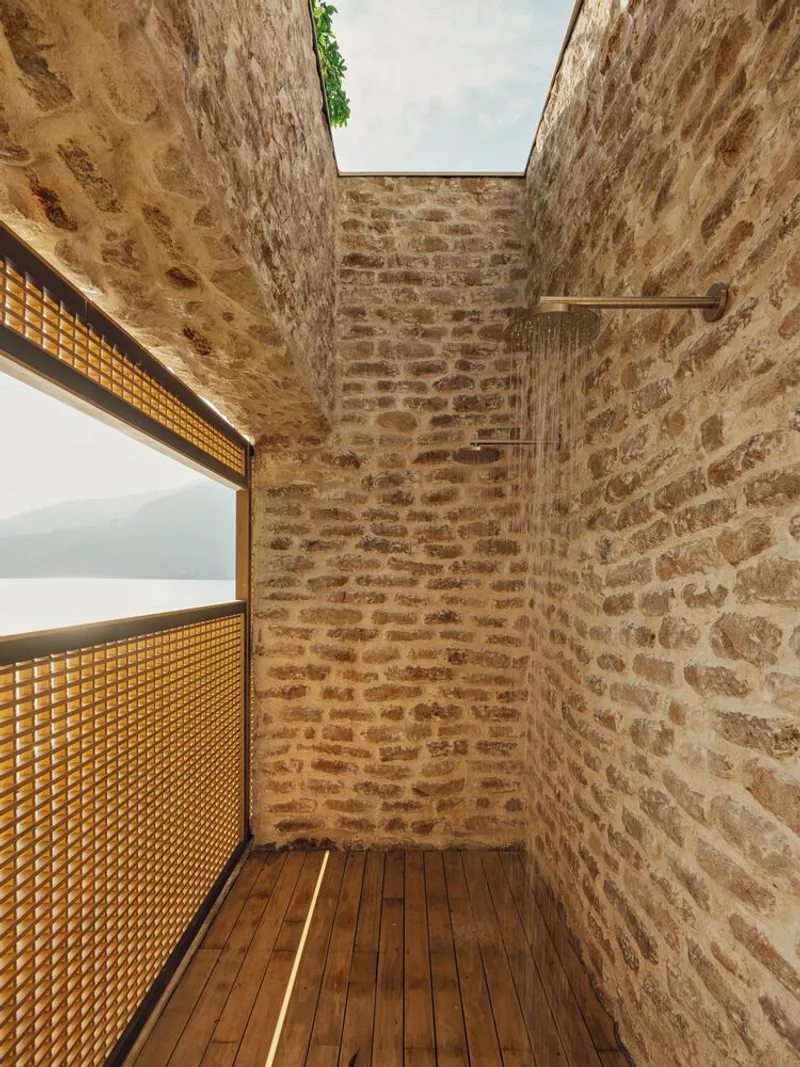 Outdoor shower enclosure with exposed stone walls, timber decking, and an open skylight above