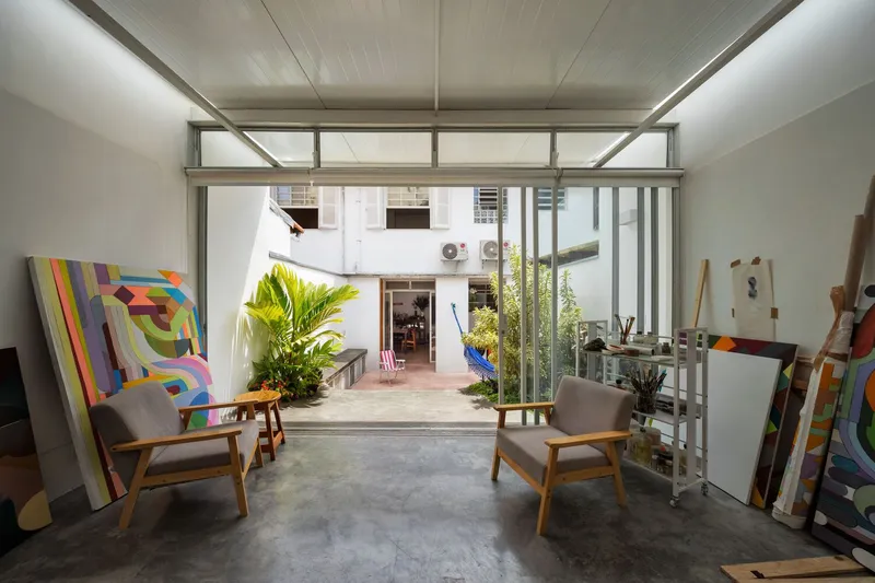 From the garden looking in: glass walls open, canvases visible inside, tree and planting in the foreground