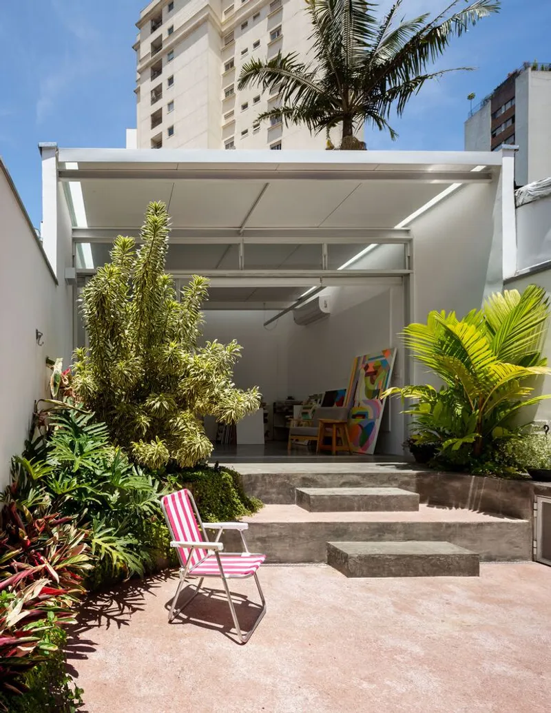 Garden with pink deck chair: tropical planting, concrete steps, atelier behind with steel canopy