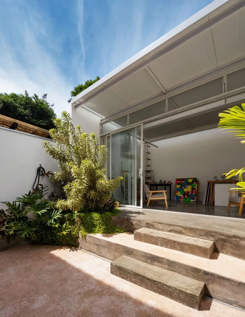 Side approach: concrete steps from garden up to the atelier level, sliding glass open, paintings inside