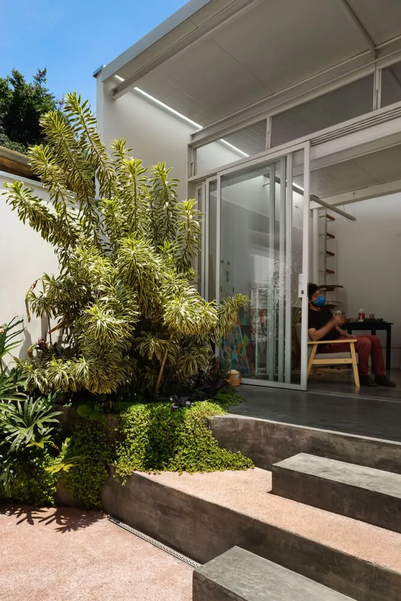 Entry from street: plywood pivot door open, view through the house to the backyard garden and atelier beyond